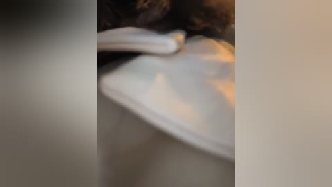 A blurred video shows a white object, possibly a laptop, resting on a black surface with a dark, textured fabric in the background. The image has a muted color palette and appears out of focus.