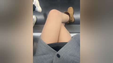 Video of a person's legs and feet in a gray blazer, tan suede boots, and beige socks, seated in a dark-colored airplane seat.