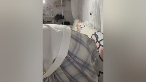 Video of a child sleeping on a white bed with a plaid blanket, wearing a white top and pink pajamas. The room is tidy with a white curtain and white furniture, giving a cozy, clean feel.