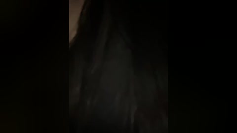 A dimly lit video featuring a person with long, dark hair, partially obscured by shadows, creating a mysterious and moody atmosphere.