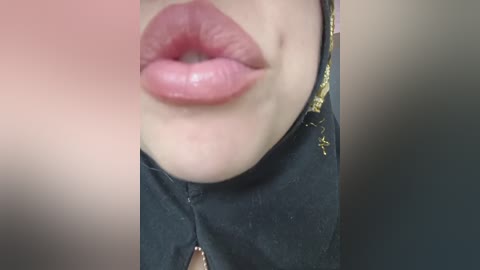 Close-up video of a woman's lips, slightly parted, with smooth, glossy pink lipstick. Her skin is fair, and she wears a black choker with gold accents. Background is out of focus.