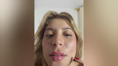 Video of a close-up of a young woman with light skin, blonde hair, and a slight smile, her face partially obscured by a blurred, tan-colored object.