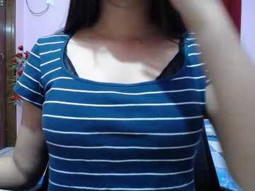 Video of a woman with long black hair, wearing a blue and white striped short-sleeved top, standing in a room with a bed and pink walls.