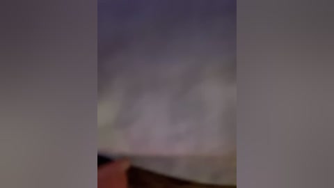 Blurry, indistinct video of a person in a dimly lit room, possibly a bedroom, with a white bed and a purple wall.