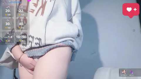 Video of a light-skinned person in a white, patterned sweater, lifting it to reveal their semi-erect penis. The background is a plain blue wall with a red heart icon and a text overlay of \"24.2\" and \"10:50.\