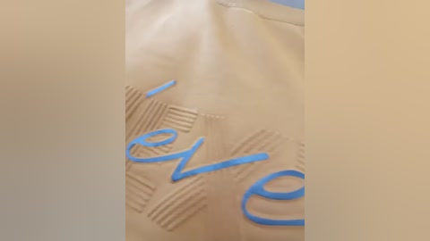 Video of a beige leather jacket with blue text \"hello\" embossed in a stylish, modern font. The jacket features subtle, horizontal lines and a smooth, polished texture.