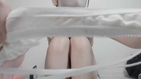 A close-up video of a woman's legs in white underwear, viewed from above, against a blurred white background.