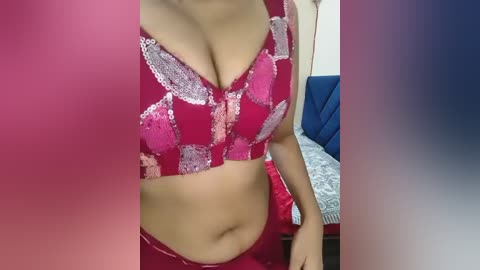 A video of a woman in a red sequined bra and matching panties, showcasing her medium-sized breasts and light brown skin. The background features a bed with blue and white bedding.