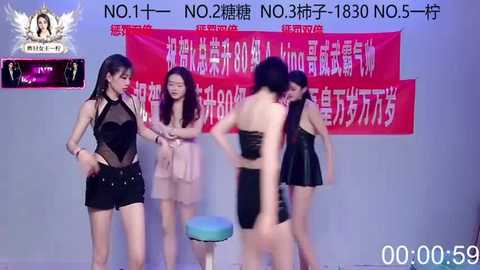 Video of four Asian women in revealing, black, sheer outfits, standing against a red banner with Chinese text. They appear in a studio setting, likely a fashion or beauty event.