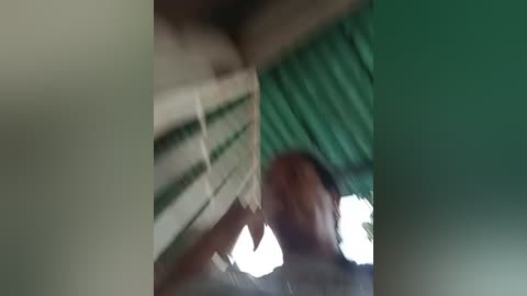 Media: A blurry video shows a man with a medium complexion and short hair, wearing a dark shirt, standing in a green-tiled room with a white ceiling fan.