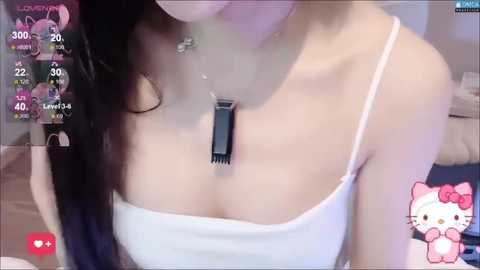 Video of a light-skinned woman with long dark hair, wearing a white spaghetti-strap tank top, necklace, and a black scarf, in a cozy room with a My Melody plush toy.