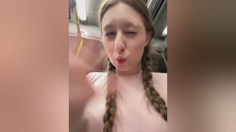 A video captures a young woman with light skin and braided brown hair, puckering her lips in a playful manner while seated on a subway train.