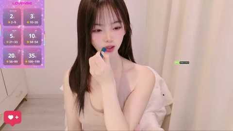 A young Asian woman with long black hair, fair skin, and a slender physique, sits in a white room, applying blue lipstick. A game interface with stats is in the top left.