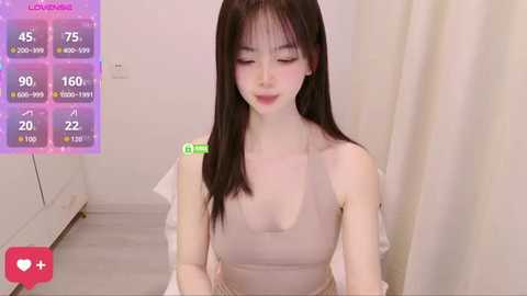 Video of an Asian woman with long black hair, fair skin, wearing a beige top, in a simple room with a \"Love Live!\" digital background.