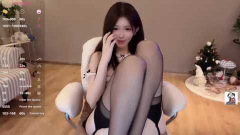 Media: Video of an Asian woman with long, dark hair, wearing black lingerie and sheer stockings, sitting in a white chair, surrounded by Christmas decorations and a TV screen displaying live streaming details.
