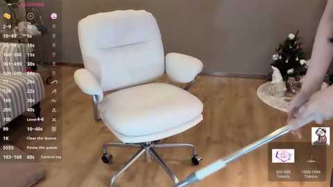 Video of a white leather office chair on a wooden floor in a room with a beige wall and a small Christmas tree. A person is adjusting the chair's height.