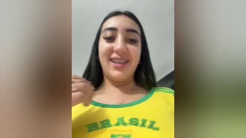A blurry video of a young woman with long black hair, light skin, and a slight smile, wearing a yellow Brazil soccer jersey.