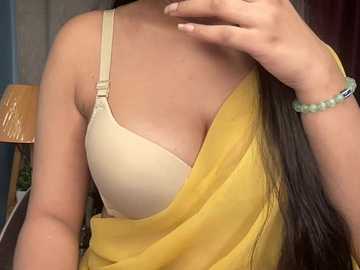 Video of a woman with medium brown skin, wearing a beige bra under a yellow off-shoulder dress. Her long, dark hair cascades down her back.