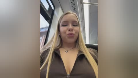Video of a blonde woman with fair skin, wearing a low-cut brown top, making a kissy face in a bus.
