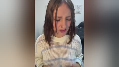 A video of a young girl with fair skin, shoulder-length brown hair, and a white knit sweater, looking sad and distressed.