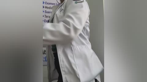 Video of a person in a white lab coat, arms crossed, standing in a white-walled room with a sign listing \"Examen, Modern, Sur, Terra, Examen, Examen, Examen, Examen, Examen, Examen, Examen, Examen, Examen, Examen, Examen, Examen, Examen, Examen, Examen, Examen, Examen, Examen, Examen, Examen, Examen, Examen, Examen, Examen, Examen, Examen, Examen, Examen, Examen, Examen, Examen, Examen, Examen, Examen, Examen, Examen, Examen, Examen, Examen, Examen, Examen, Examen, Examen, Examen, Examen, Examen, Examen, Examen, Examen, Examen, Examen, Examen, Examen, Examen, Examen, Examen, Examen, Examen, Examen, Examen, Examen, Examen, Examen, Examen, Examen, Examen, Examen, Examen, Examen, Examen, Examen, Examen, Examen, Examen, Examen