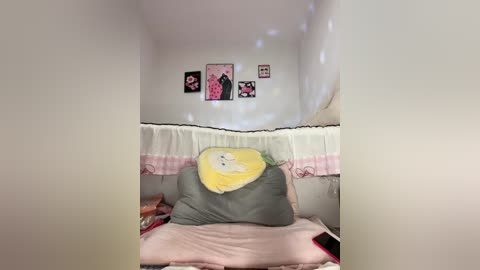 A video of a cozy, white-walled bedroom with a small window and soft, pastel decor including a yellow pillow, white quilt, and framed art.