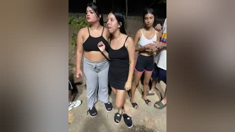 Video of three young women in casual sportswear, standing outdoors at night, with a blurred background.