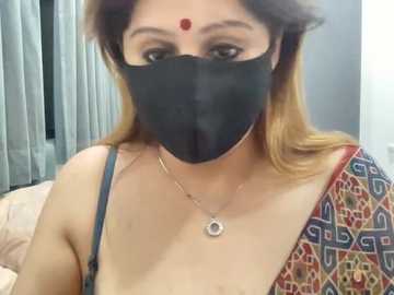 A video of a South Asian woman with light brown skin, wearing a black mask, red bindi, and traditional attire with intricate embroidery.