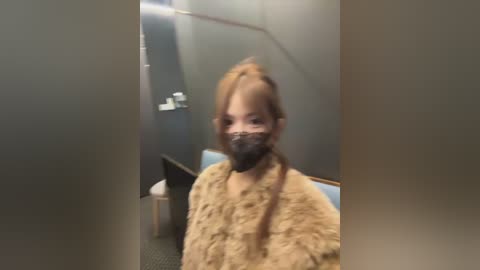 Video of a woman in a beige fur coat and black mask standing in a dimly lit, narrow hallway with a metal staircase.