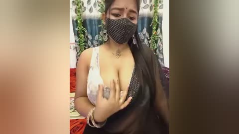 Video of a South Asian woman with medium brown skin, wearing a white blouse, black mask, and black saree, showing cleavage, indoors.
