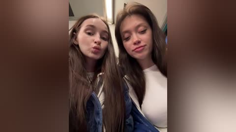 Video of two young women, one with long brown hair and denim overalls, the other with straight brown hair and a white top, puckering their lips in a playful kiss.