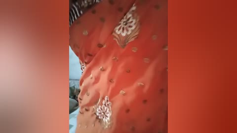Video of a close-up of a woman's torso, wearing a peach-colored blouse with white floral embroidery. Background is a gradient of orange to red.