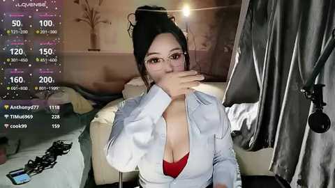 Video of a young Asian woman with glasses, wearing a white denim jacket and red bra, blowing smoke into the camera, in a dimly lit bedroom with a bed and a TV.