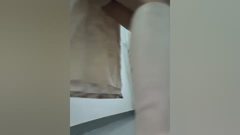 A blurred video of a partially visible, naked person standing in a dimly lit, narrow hallway with beige walls. The person\u2019s torso and legs are faintly discernible, with a white towel draped over their shoulders.