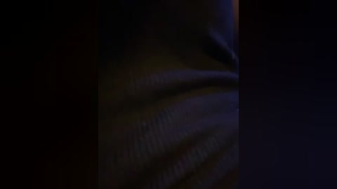 A dimly lit video of a human hand, partially in shadow, with visible wrinkles and ridges on the skin, emphasizing the texture.