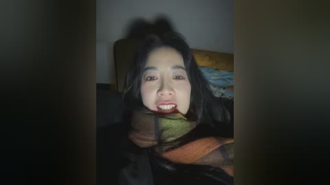 Video of an Asian woman with long black hair, smiling, lying on a bed with a green pillow, blurred background.