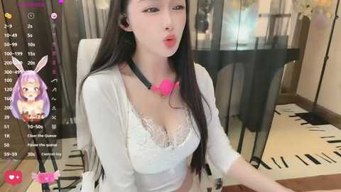 Video of an Asian woman with long black hair, wearing a white lace bra, pink bunny ears, and a black choker. She's seated at a table in a modern indoor setting with a live-stream overlay.