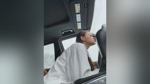 Video of a young woman in a white shirt, leaning forward with eyes closed, seated in a car with a fogged-up window, blurry background.