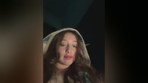 Video of a young woman with long, curly brown hair, wearing a hooded cloak, with a soft, diffused lighting creating a mysterious, slightly blurred background.
