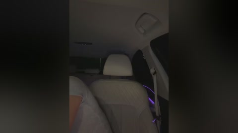Video of a dimly lit car interior, showing a white headrest, beige seat, and purple ambient lighting. The image is slightly blurry, giving a sense of motion.