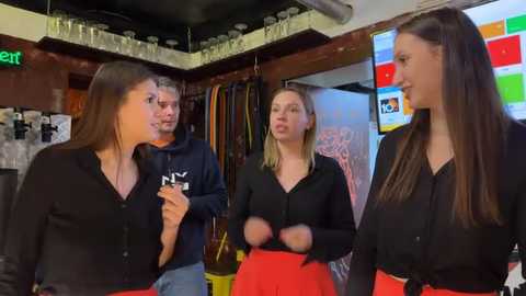 Video of four young women in a cozy, dimly-lit bar; one wears a black shirt and red skirt, another a black shirt and beige pants, and two others in black shirts.