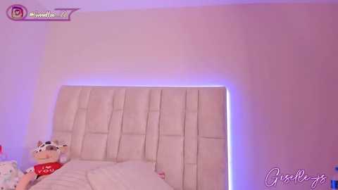 Video of a plush teddy bear and a bed with a tufted white headboard and purple accent lighting.