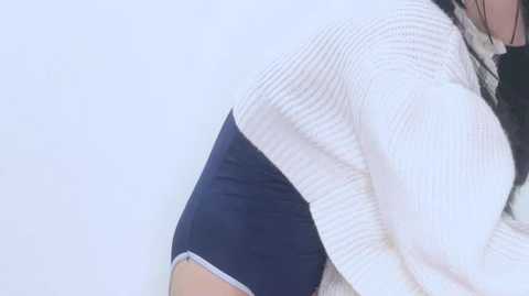 Close-up video of a person wearing a white ribbed sweater with a blue sleeve, likely a man, against a plain white background.
