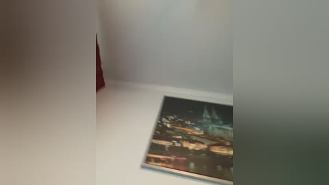 A video captures a corner of a room with white walls, a red-painted section, and a framed video of a nighttime cityscape. The image is slightly blurred, giving it a soft, dreamy feel.