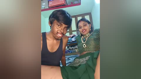 A video of a man in a black tank top, with short dark hair, and a woman in a green sari, standing indoors.