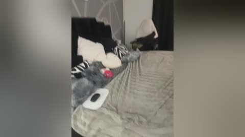 A blurry video of a messy bedroom with a black-and-white striped comforter, grey blanket, and scattered stuffed animals, including a red bear.