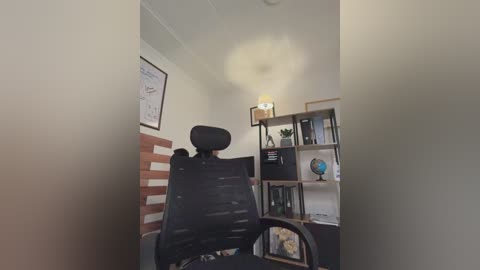 Video of an empty, modern office with a black ergonomic chair facing a whiteboard wall. The room features a bookshelf, a globe, and a lamp on a metal stand.