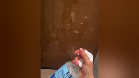 Video of a person holding a water bottle in front of a smudged mirror, reflecting a blurred image of a person in the background.