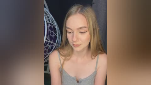 Video of a young Caucasian woman with long blonde hair, wearing a light gray tank top, standing indoors near a hanging air hockey table.