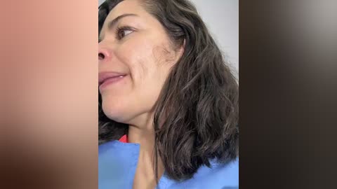 Video of a woman with shoulder-length dark hair, fair skin, and light makeup, wearing a blue top, smiling. The background features a blurred gradient from pink to black.